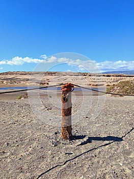 Fence of round wooden posts attached with a rope to delimit the path.Wooden post in desert landscape with lagoon and blue sky.