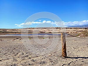 Fence of round wooden posts attached with a rope to delimit the path.Wooden post in desert landscape with lagoon and blue sky.