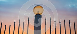 Fence with sharp peaks and street lamp in the evening. Street lamp on the background of a beautiful sunset sky