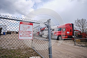 Fence with a sign of protection and video surveillance and Several old trucks stand in the parking lot. Version 3