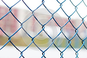 Fence on the sky, blue mesh fence, chain link fence, building back background. Soft focus.