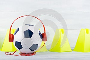 Fence yellow cones on a gray background, behind a soccer ball, which is wearing red headphones