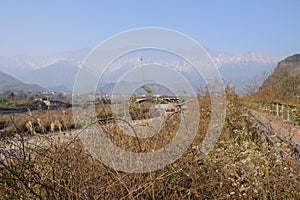 Fenced jogging path in weeds along dried riverway before broken bridge with jokul in distance