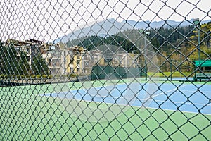 Fenced tennis court before houses in mountains