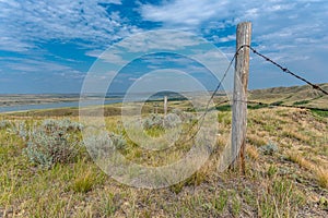 A fencepost with grasslands and Diefenbaker Lake in the Saskatchewan Landing Provincial Park in background