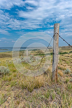 A fencepost with grasslands and Diefenbaker Lake in the Saskatchewan Landing Provincial Park in background