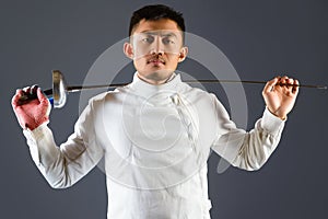 Fencing athlete posing with a sword or epee on gray background