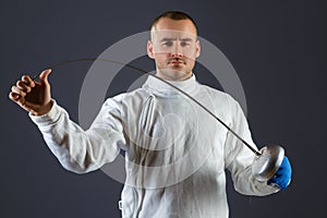 Fencing athlete posing with a sword or epee on gray background