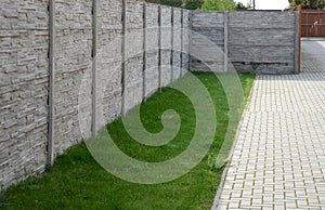 Fencing with a gray panel fence in the garden with a lawn and concrete interlocking paving. A panel fence is the best protection a