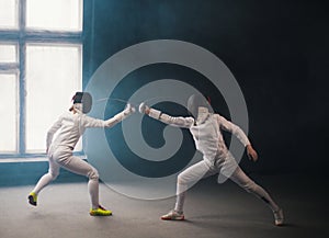 A fencing training in the studio - two women in protective costumes having a duel - poking with a swords in each other photo