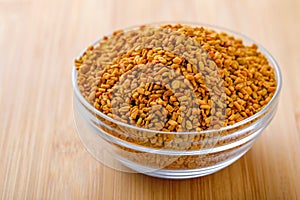 Fenugreek seeds in glass bowl and scoop on wooden background