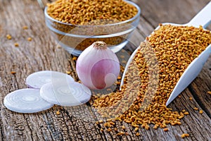 Fenugreek seeds in glass bowl and scoop on wooden background