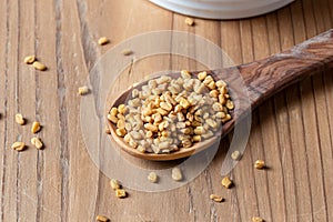 Fenugreek seeds on a wooden spoon on a table