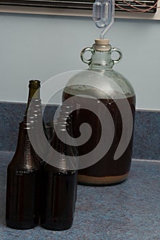 Fermented beer in a demijohn with airlock and dark bottles in kitchen