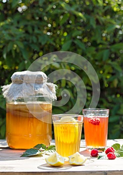 Fermented drink Kombucha in a glass jar and two glasses with a drink with lemon and raspberry in the foreground.
