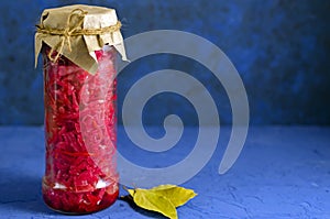 Fermented pickled vegetables. red cabbage with beets and bay leaves in a glass tall jar on a classic blue background