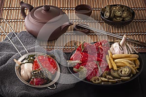 Fermented red and green hot peppers and garlic on a straw mat background with chopsticks and a teapot.