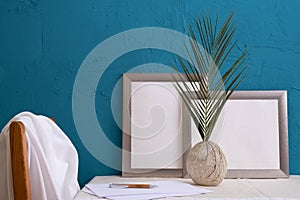 Fern in an old vase, a set for writing, two gray frames for a photo on a blue background