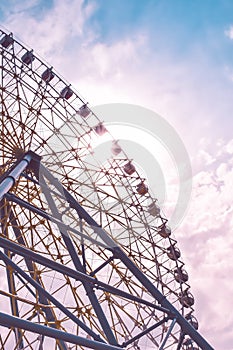 Ferris wheel in the amusement park photographed against the sun. Construction of the attraction with pink sky and clouds