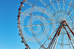Ferris wheel in the amusement park photographed against the sun. Construction of the attraction with pink sky and clouds