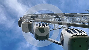 Ferris wheel with closed metal booths slowly rises against the blue sky, bottom view