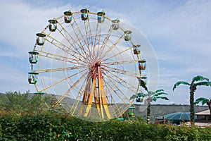 Ferris wheel with colorful booths, against a blue sky with white clouds.