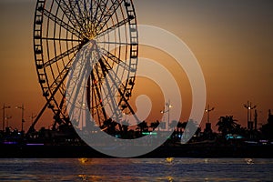 Ferris wheel and Georgian alphabet tower on orange sunset background.