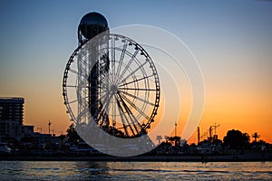 Ferris wheel and Georgian alphabet tower on orange sunset background.