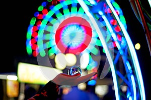 Ferris wheel through a glass ball on the palm of your hand. The atmosphere of celebration and rest. Evening adventure