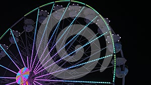 Ferris wheel at night. The multi-colored Illuminated wheel spins and rolls vacationers in its white booths