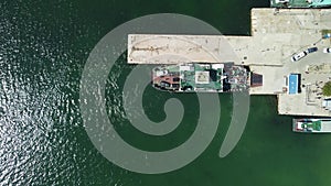 Ferry boat crossing the sea, carrying cars and passengers. Cars drive off the deck onto the port. Top-down aerial drone