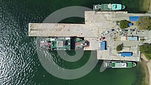 Ferry boat crossing the sea, carrying cars and passengers. Cars drive off the deck onto the port. Top-down aerial drone