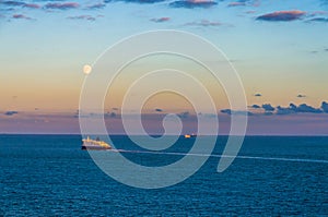 Ferry crossing the sea at sunset under a full moon