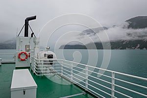 Ferry deck view to the fjord mountains in clouds and fog.