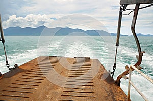 Ferry ramp and trace on the water of tropical sea behind ferry, with tropical Koh Chang island on horizon in Thailand