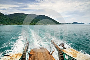 Ferry ramp and trace on the water of tropical sea behind ferry, with tropical Koh Chang island on horizon in Thailand