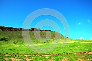 Fertile pasture on the slope of a high hill with the remains of ancient buildings at the top