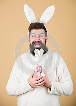 Fertile and prolific. Hipster with long rabbit ears holding egg laying hare. Easter bunny delivering colored eggs