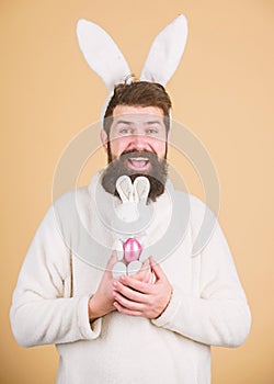 Fertile and prolific. Hipster with long rabbit ears holding egg laying hare. Easter bunny delivering colored eggs