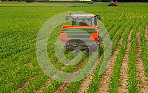 Fertiliser spreader machine trailed by tractor on a field with young corn plants