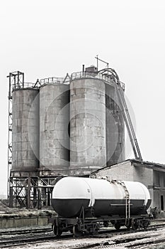 Fertilizer chemical tank on the rails of the railway industrial station against the background of old sand storage tanks at an