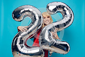 a fervently laughing, emotional woman in a red shirt stands on a blue background and holds inflatable balloons in the