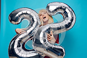 a fervently laughing, emotional woman in a red shirt stands on a blue background and holds inflatable balloons in the