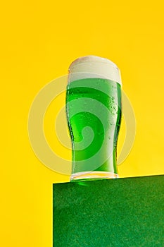 Festival drink. Glass of foamy frothy green beer over bright yellow background. Traditional taste. Concept of st