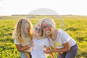 Festival of holi, friendship, happiness and holidays concept - Happy and funny girls covered in paint in green field