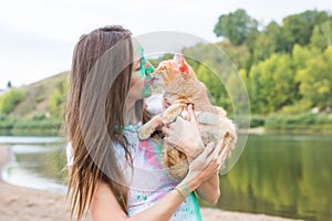 Festival holi, holidays, tourism and nature concept - young woman dressed in white shirt holding cat and covered with