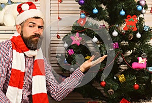 Festivals and decor concept. Guy in hat decorates fir tree