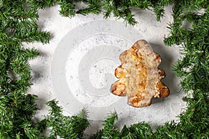 Festive almond pastry in christmas tree shape surrounded by greenery on snowy background