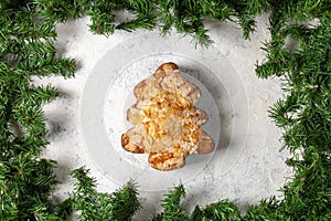 Festive almond pastry in christmas tree shape surrounded by greenery on snowy background