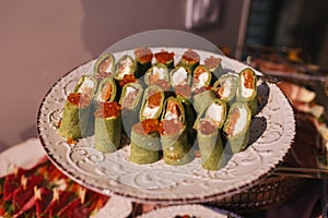 Festive appetizers on receptions. Spinach crapes rolls with caviar, salmon and cream cheese inside. Plate with savoury